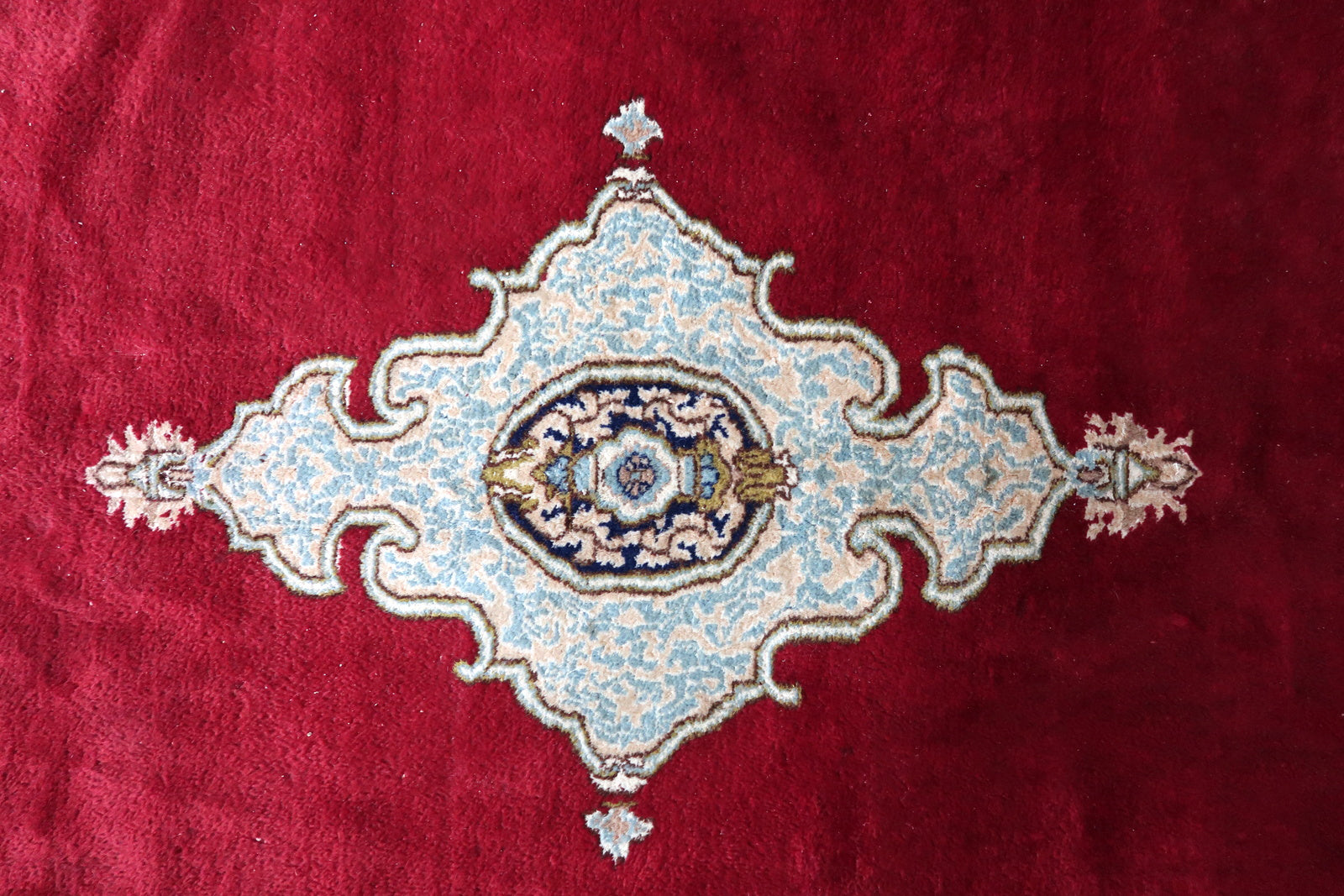 Full view of an antique Persian Kerman rug laid flat, showing its rectangular shape, vast plain crimson ground with only medallion and pendant, wide ivory inner border, and bold deep navy outer arcade border.

