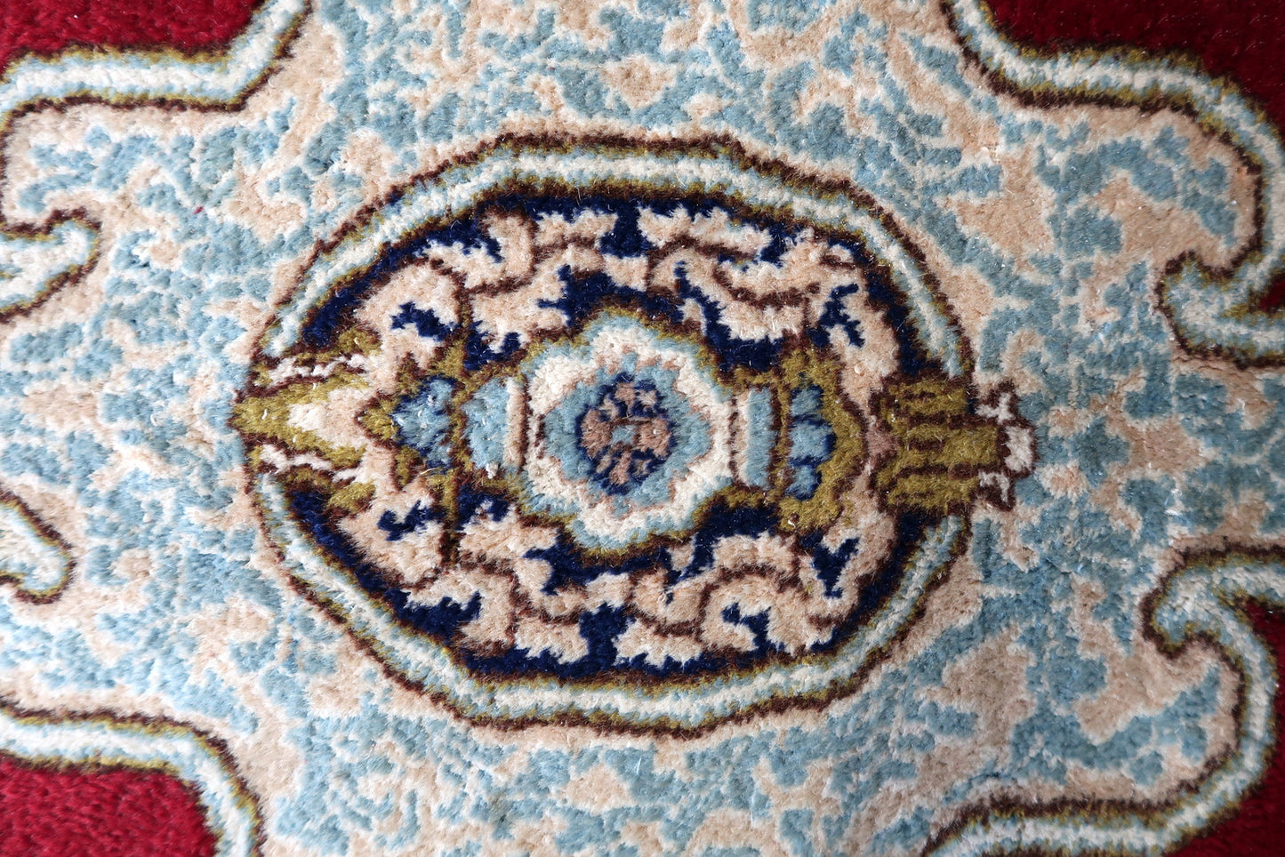 Close-up of the corner of a 1930s Kerman rug, revealing the transition from the open crimson field to the multi-layered border system – ivory inner floral scroll, pink guard strip, and deep navy arcade main border.

