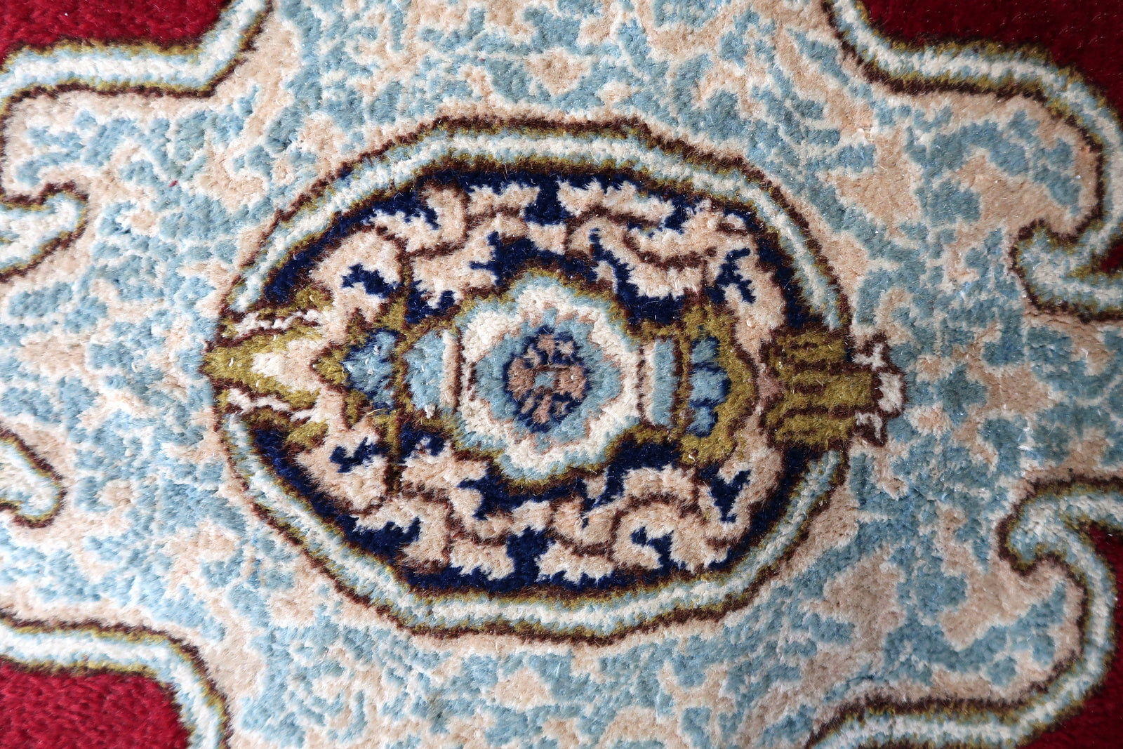 Close-up of the corner of a 1930s Kerman rug, revealing the transition from the open crimson field to the multi-layered border system – ivory inner floral scroll, pink guard strip, and deep navy arcade main border.

