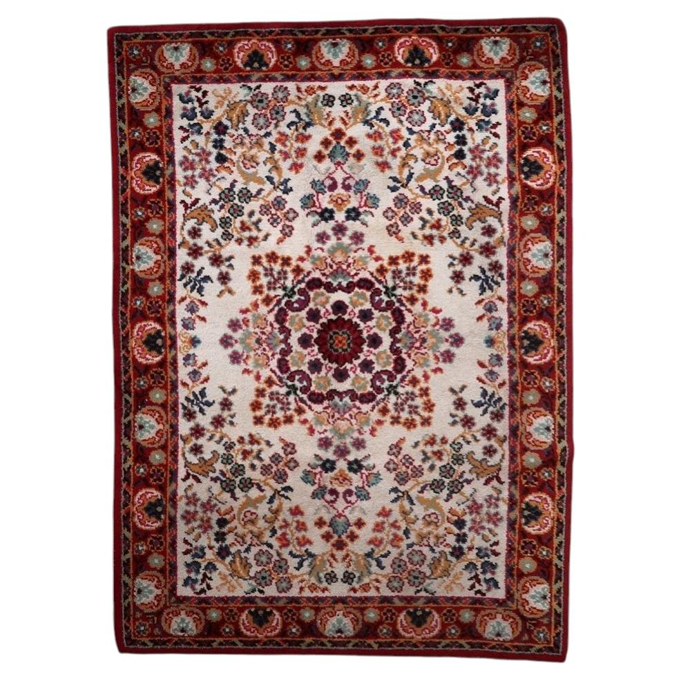 Full view of a vintage French Savonnerie-style rug from the 1950s, featuring an open luminous ivory/cream field with a large multi-lobed crimson rosace medallion surrounded by scattered floral bouquets (roses, carnations, gold sprays, pink accents), framed by a wide deep crimson border – measuring 6.7 × 9.6 feet.

