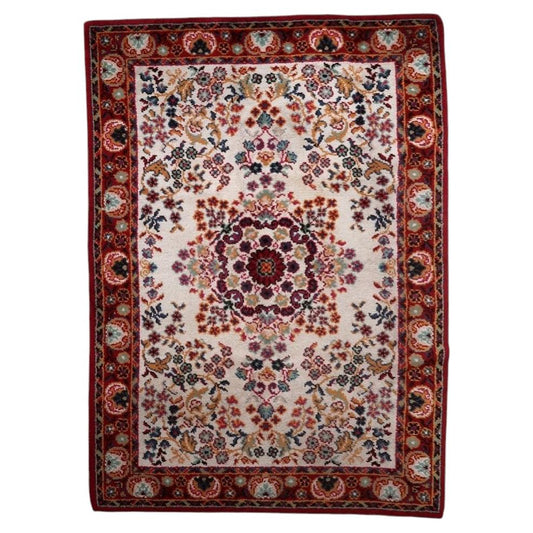 Full view of a vintage French Savonnerie-style rug from the 1950s, featuring an open luminous ivory/cream field with a large multi-lobed crimson rosace medallion surrounded by scattered floral bouquets (roses, carnations, gold sprays, pink accents), framed by a wide deep crimson border – measuring 6.7 × 9.6 feet.

