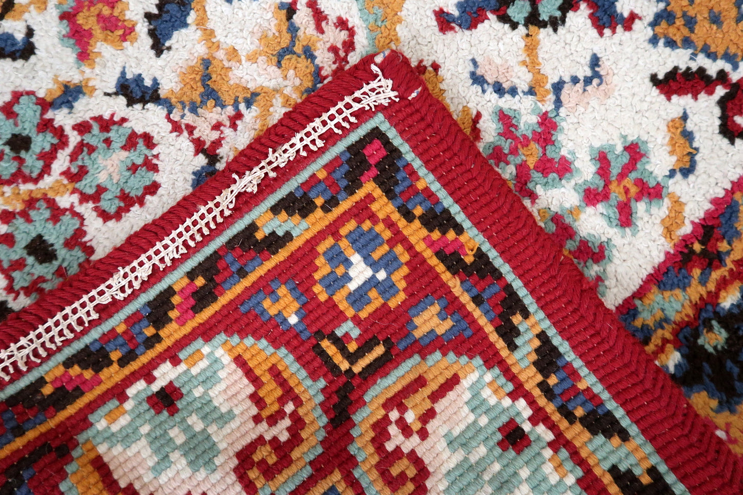 Close-up of the crimson main border on a 1950s French Savonnerie rug, revealing large ivory/cream roses and peonies with internal teal and gold detail, connected by a crimson vine with gold leaf forms and teal accents.

