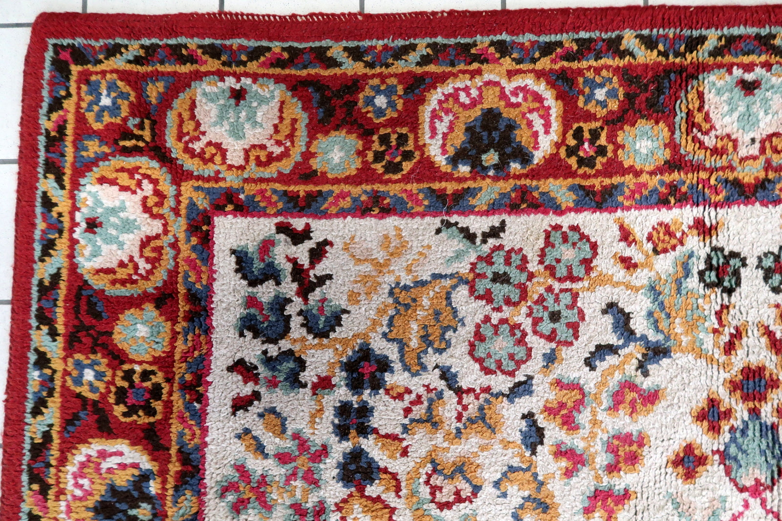 Close-up of the central medallion on a 1950s French Savonnerie rug, showing a deep crimson/ruby red center rosette with gold point, surrounded by concentric rings of dark navy scrolling acanthus forms with teal detail, and an outer ring of crimson scrolling forms with black outlines and gold accents.

