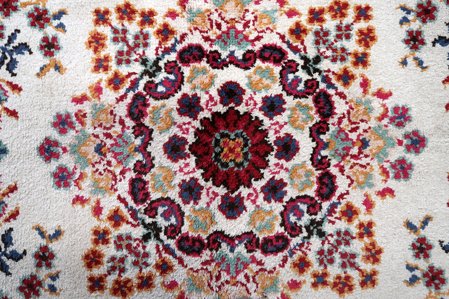 Close-up of the scattered floral bouquets on a 1950s French Savonnerie rug, showing open-faced crimson roses with teal leaf clusters, gold/amber accent flowers, and pale pink blush flowers floating independently on the warm ivory ground in the characteristic "jardin" (garden) composition.


