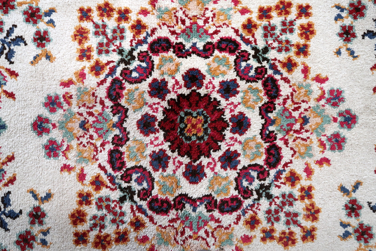 Close-up of the scattered floral bouquets on a 1950s French Savonnerie rug, showing open-faced crimson roses with teal leaf clusters, gold/amber accent flowers, and pale pink blush flowers floating independently on the warm ivory ground in the characteristic "jardin" (garden) composition.

