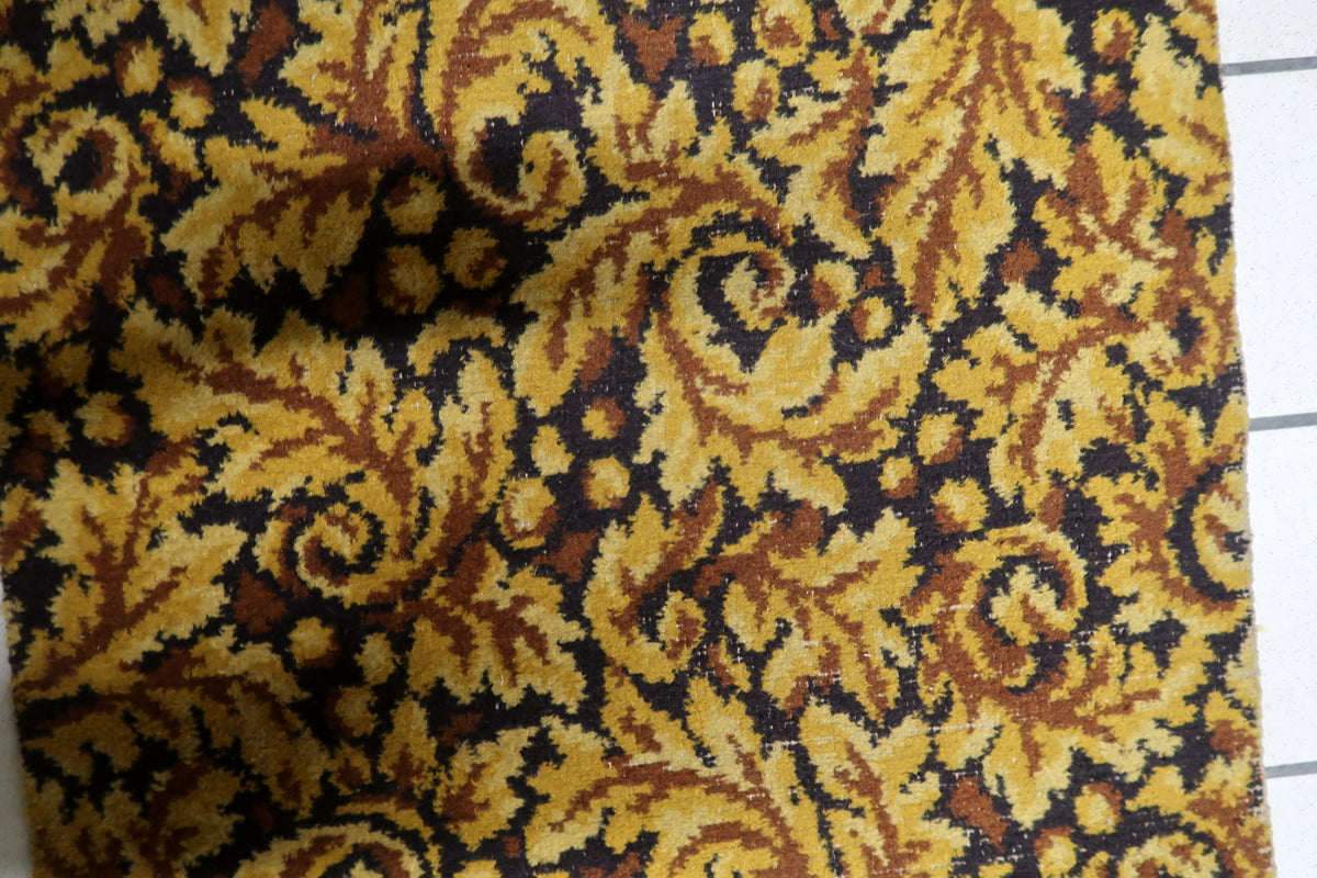 Retro 1960s acrylic accent rug displaying intricate foliate scrollwork, baroque leaf patterns, and gold-brown tonal shading.