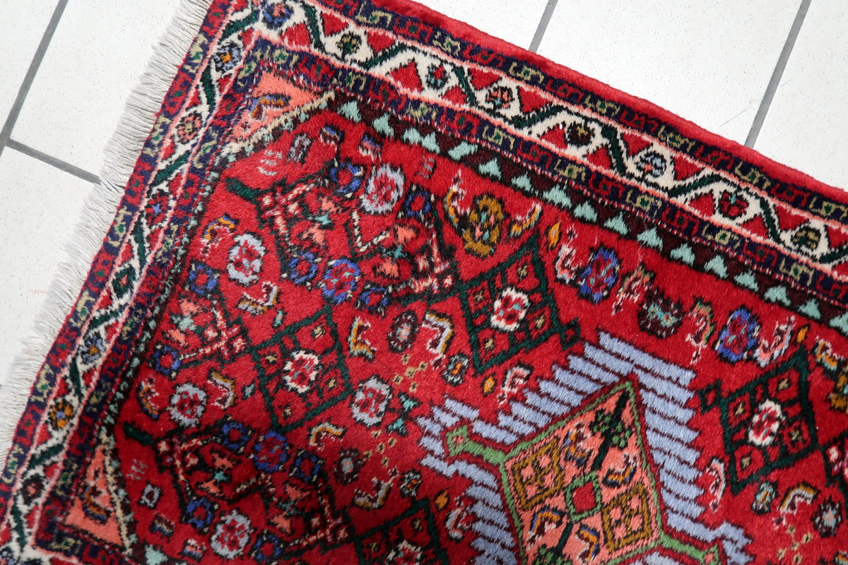 Traditional handmade rug in rich red tones with a prominent central medallion and decorative border