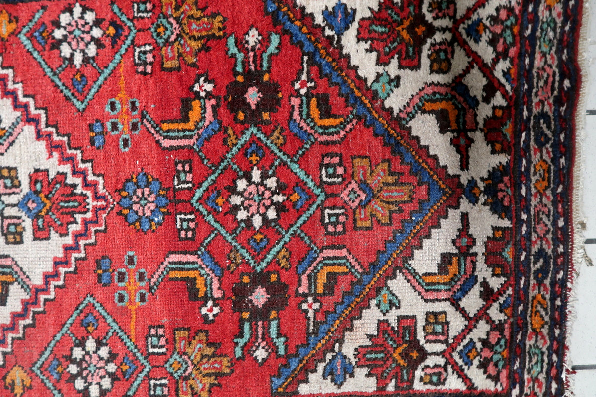 Classical floral spandrels and corner designs framing the rich red interior field of an antique 1920s carpet.
