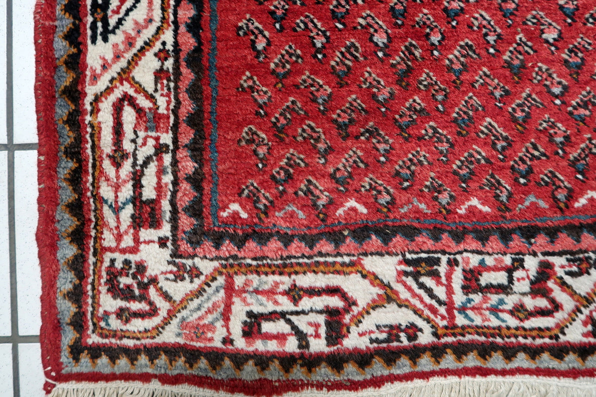 Deep crimson red, warm cream ivory, navy indigo, and subtle earth tones on a mid-20th-century handmade wool rug.