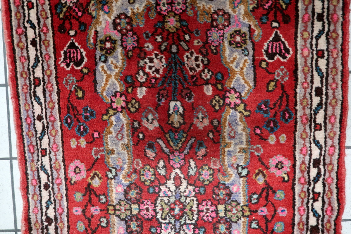 Detailed central floral medallion surrounded by delicate arabesques, palmettes, and trailing vine scrollwork on a red field.