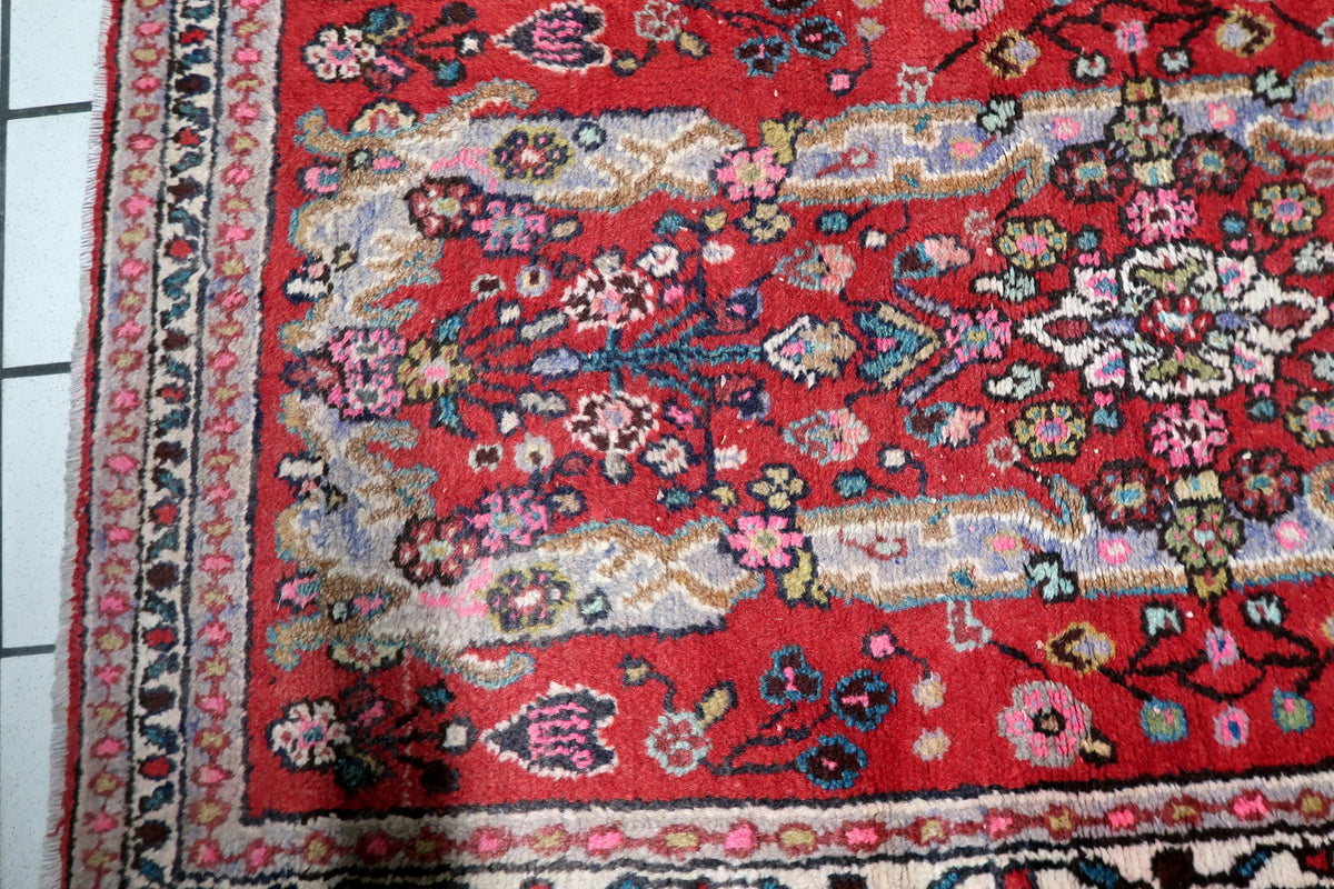 Classical corner spandrels and ornamental botanical elements framing the central red interior of a hand-knotted Indian carpet.