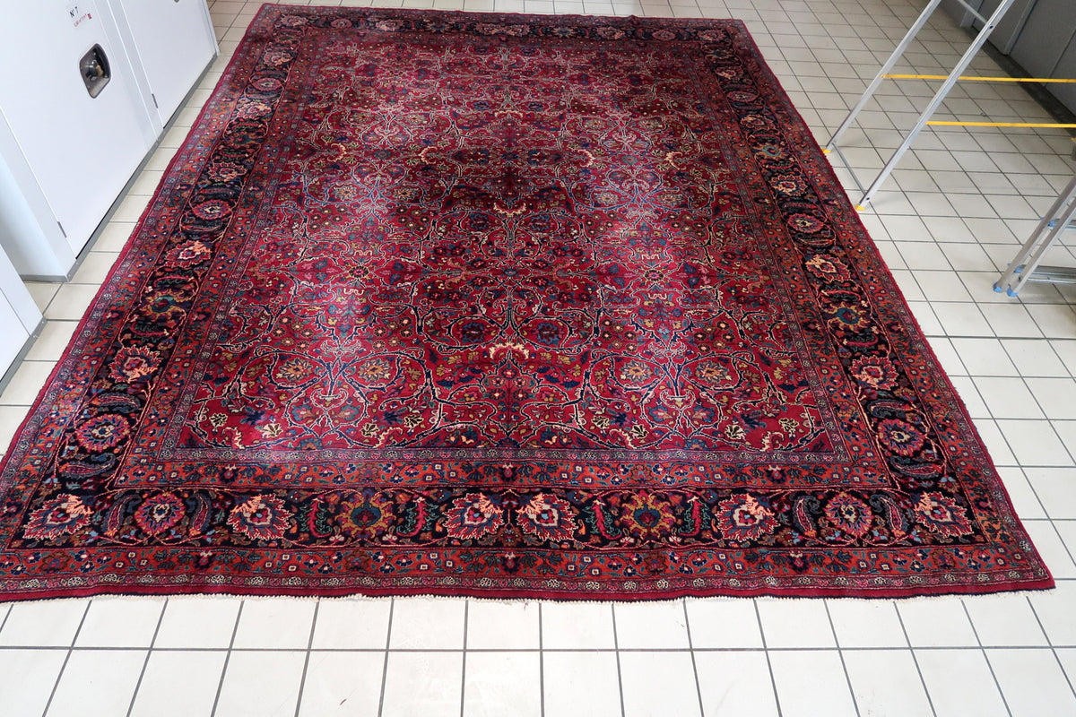 Full-length view of red wool rug with scrolling arabesques and layered floral borders