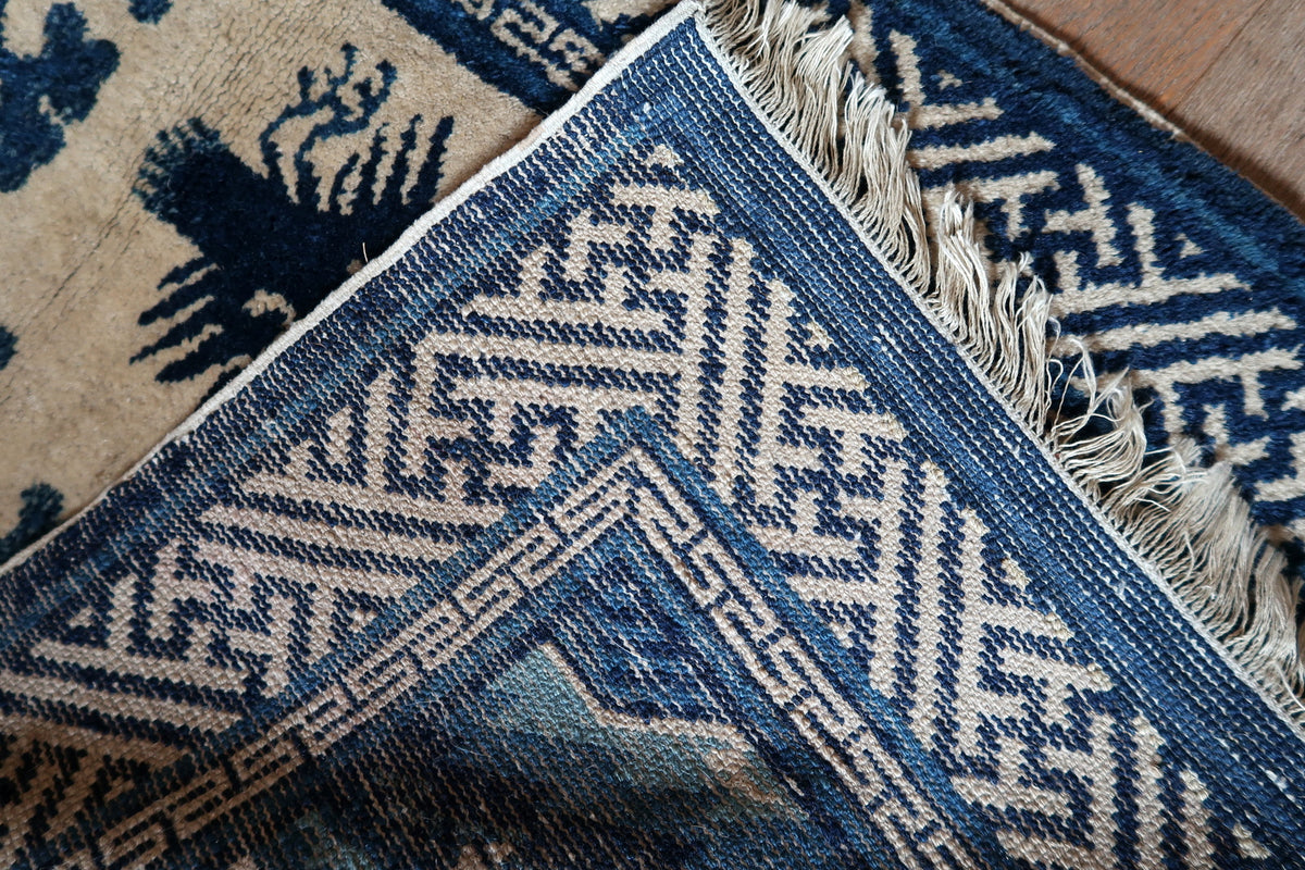Folded rug corner showing reverse weave, ivory-and-blue fretwork and uneven fringe