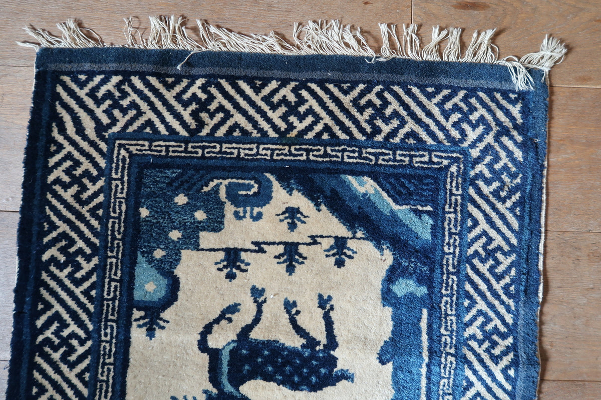 Worn light fringe and navy fretwork border above a spotted deer motif