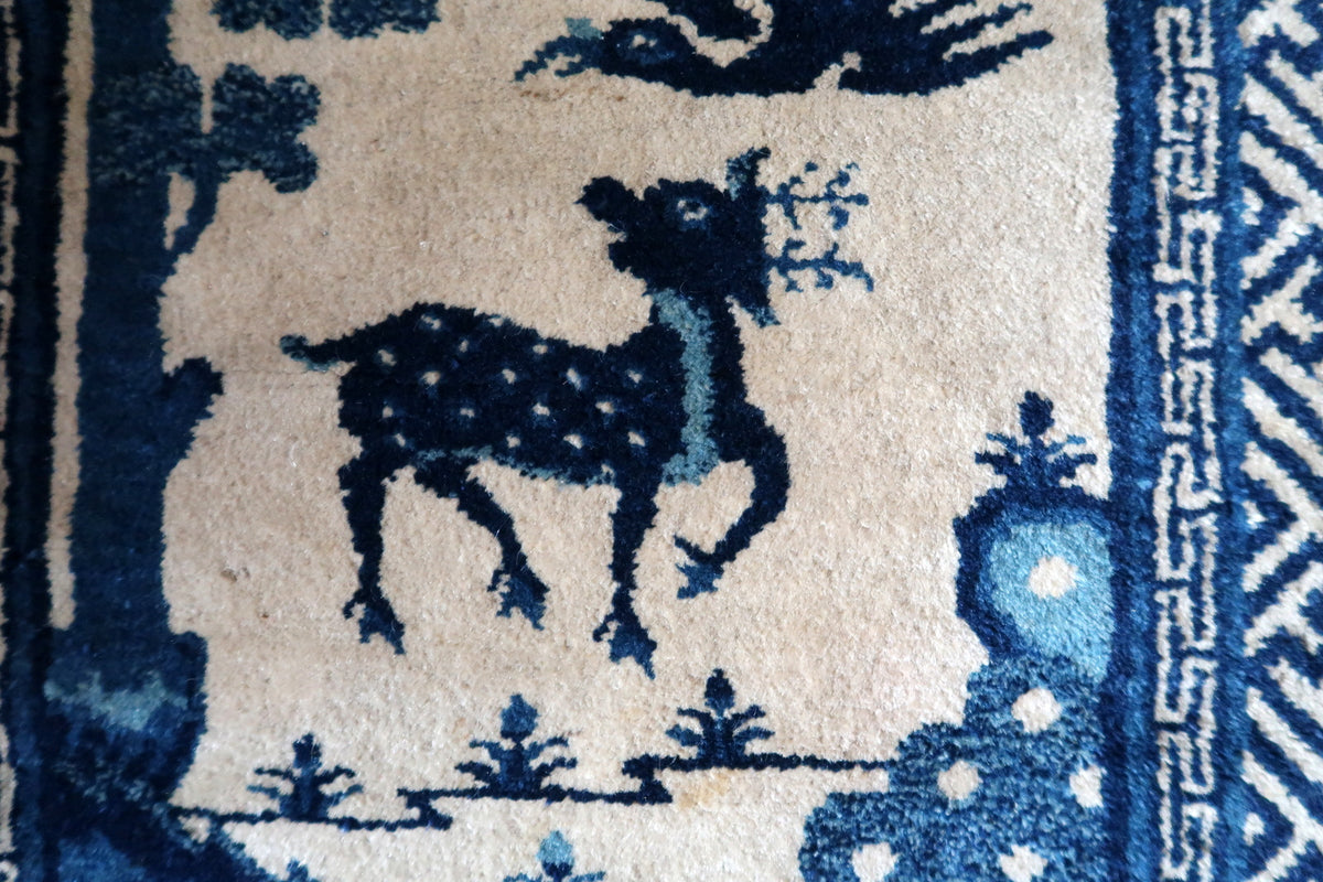 Close-up of spotted indigo deer with blue neck detail on an ivory wool field