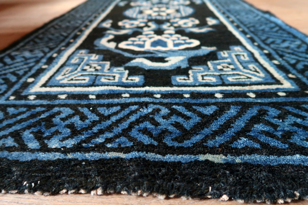 Low-angle view of wool surface, blue fretwork border and short uneven fringe remnants