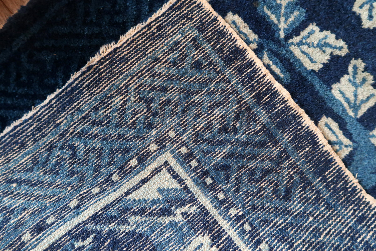 Folded rug corner showing reverse weave and blue fretwork border