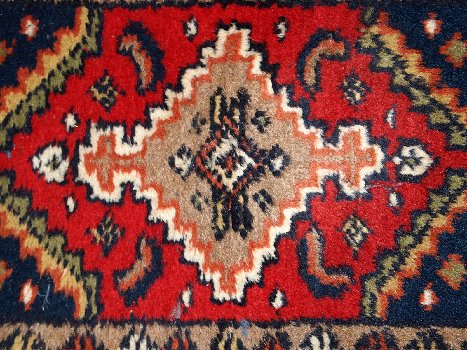 Full view of the handmade vintage rug, showcasing its vibrant background colors of red, white, and navy blue.


