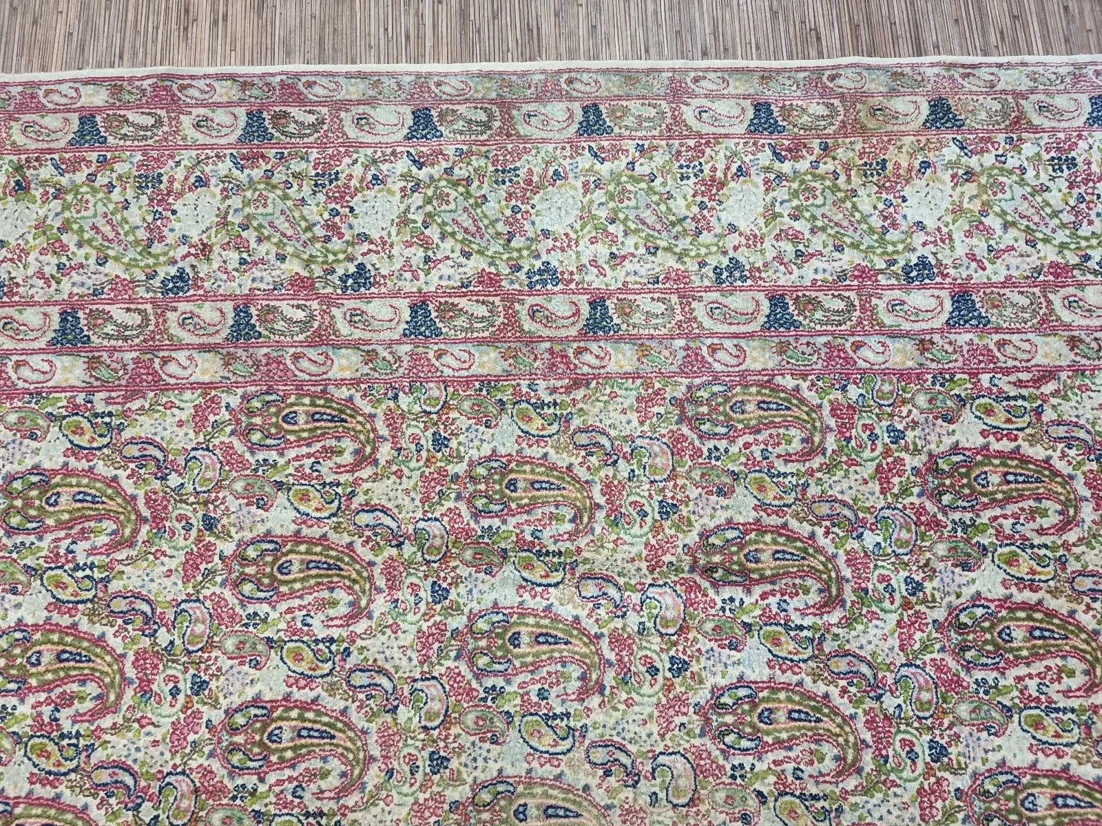 Close-up of a hand-knotted 1930s Persian Kerman carpet showing traditional floral motifs and detailed medallion design in a neutral beige palette on premium wool.

