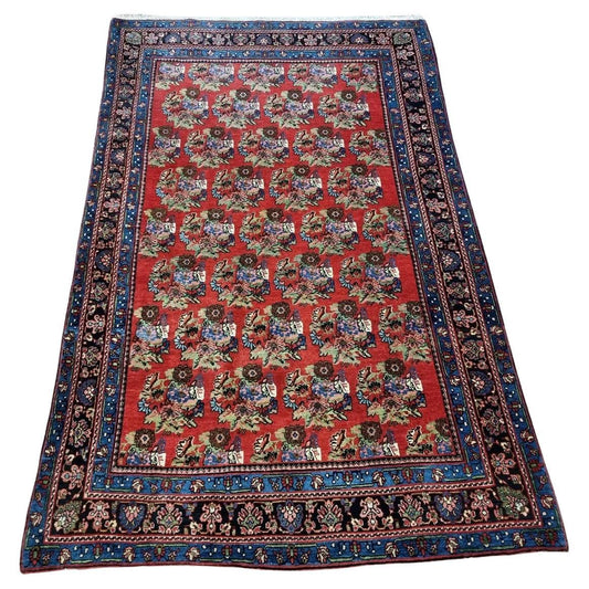 Full view of an antique Persian Bidjar rug from the early 1900s, featuring a floral design in warm rust-red tones, hand-knotted with the dense weave known as the "Iron Rug of Persia."

