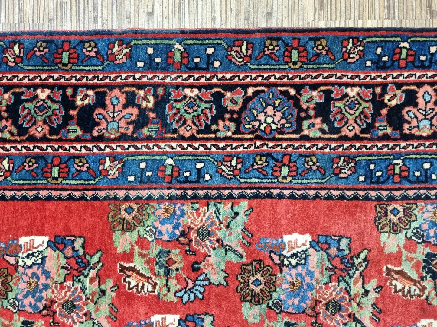 Full view of an antique Persian Bidjar rug laid flat, showing its rectangular shape, multiple borders, and classic floral medallion design in rust-red, navy, and ivory.

