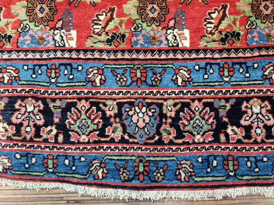 Close-up of a 1900s Persian Bidjar carpet showing elegant floral motifs and intricate detailing in rust-red, navy, and ivory on a premium wool pile with cotton foundation.

