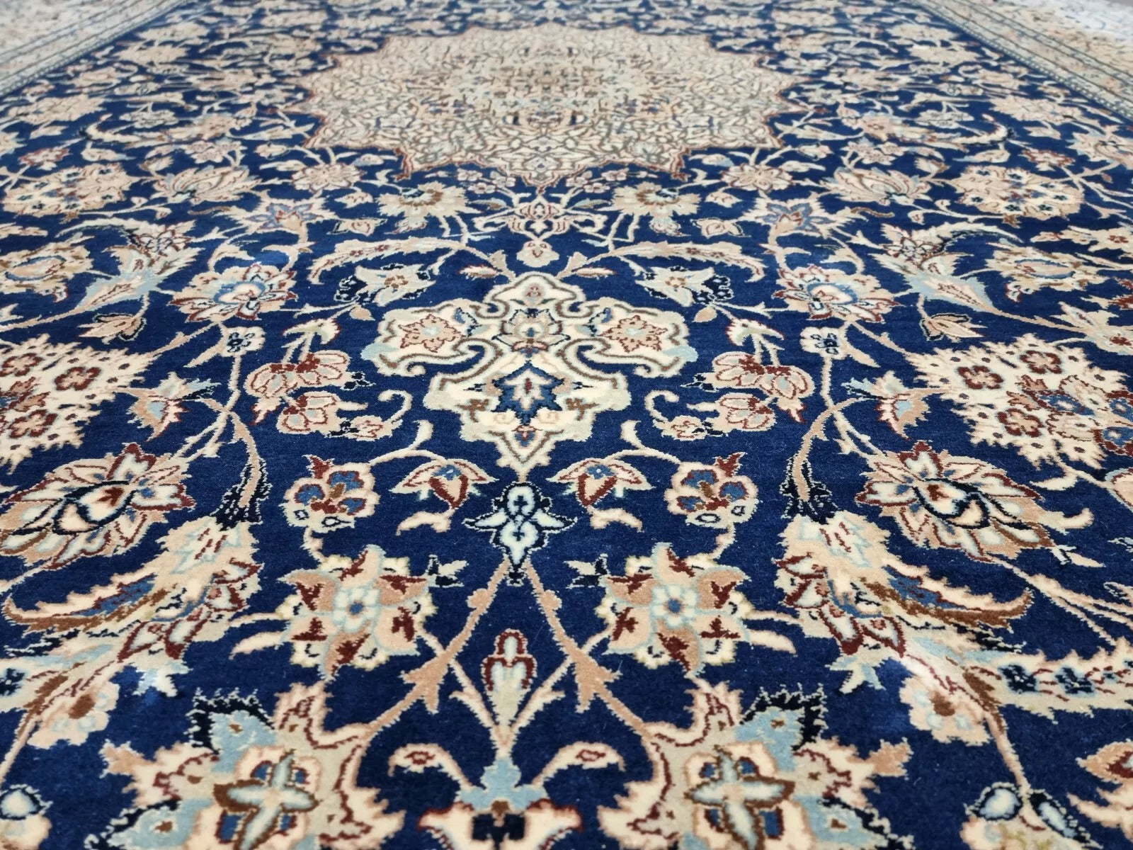 Detail of the border on a 1920s Persian Nain carpet, revealing repeated floral and vine motifs in navy and ivory with fine silk accents for added luster.

