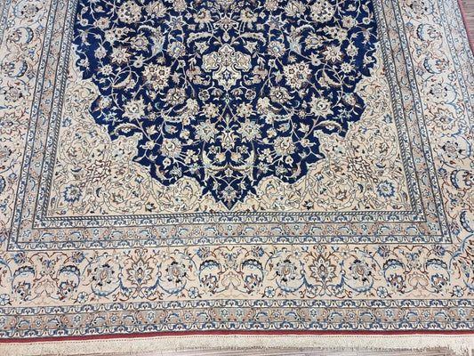 Close-up of a 1920s Persian Nain carpet showing the detailed floral and arabesque patterns in navy, blue, and beige, with the characteristic fine weave of kork wool and silk on a cotton foundation.

