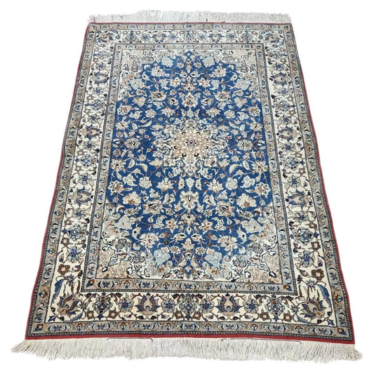 Full view of an antique Persian Nain rug from the 1920s, featuring a soft ivory field with intricate floral medallions and arabesques, hand-knotted with approximately 800,000 knots per square meter in kork wool on a cotton foundation.


