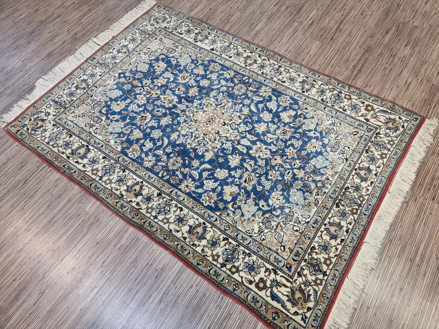 Detail of the border on a 1920s Persian Nain carpet, revealing repeated floral and vine motifs in navy, blue, and beige with fine wool texture and elegant symmetry.

