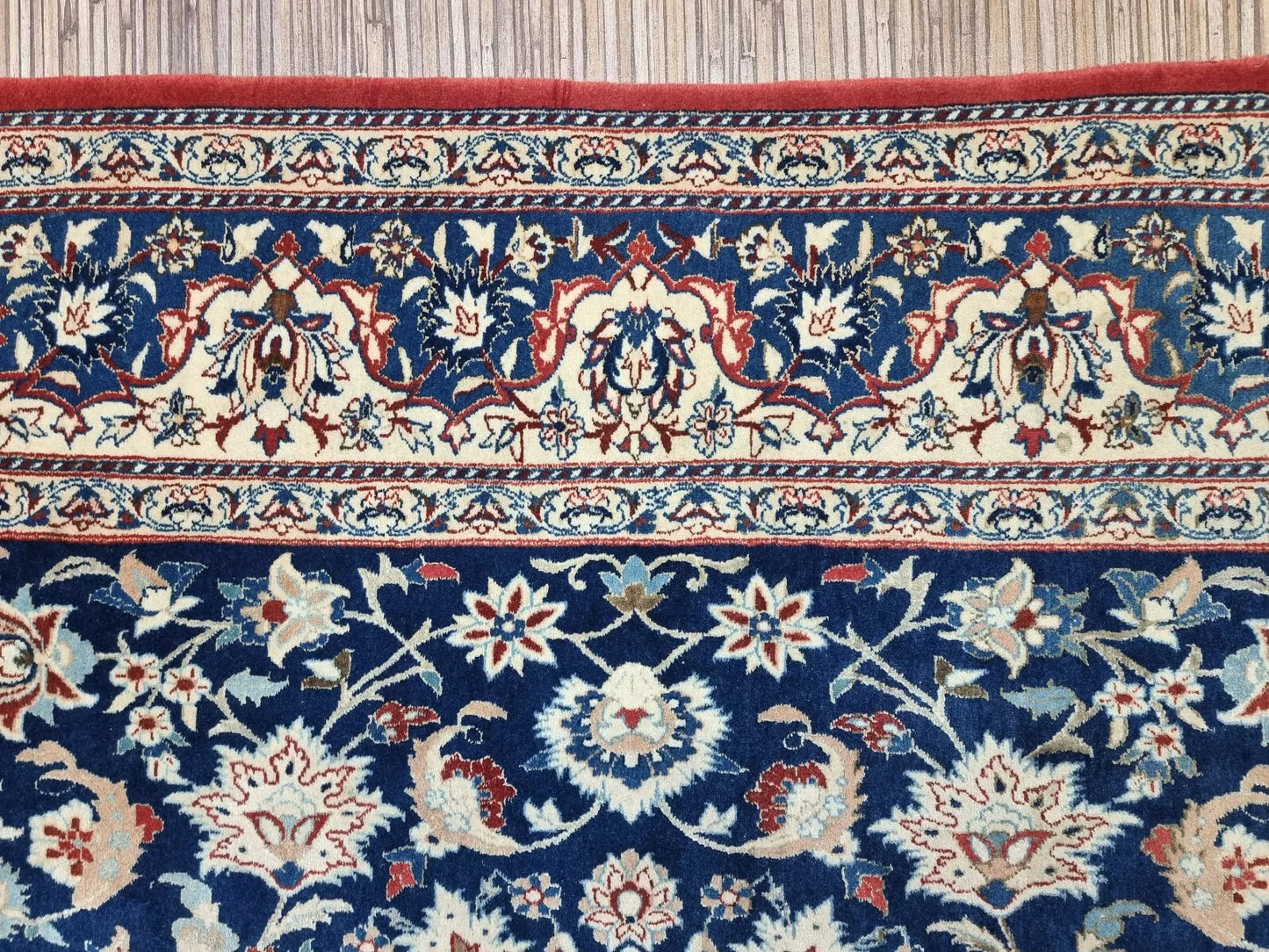 Detail of the border on a 1920s Persian Nain carpet, revealing repeated floral and vine motifs in navy, blue, and beige with fine wool texture and elegant symmetry.

