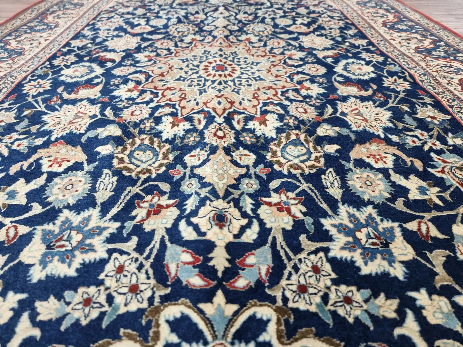 Close-up of a 1920s Persian Nain carpet showing the classic central medallion and corner spandrels with delicate floral patterns in navy, blue, and beige, with fine wool texture from high-knot-density weaving.

