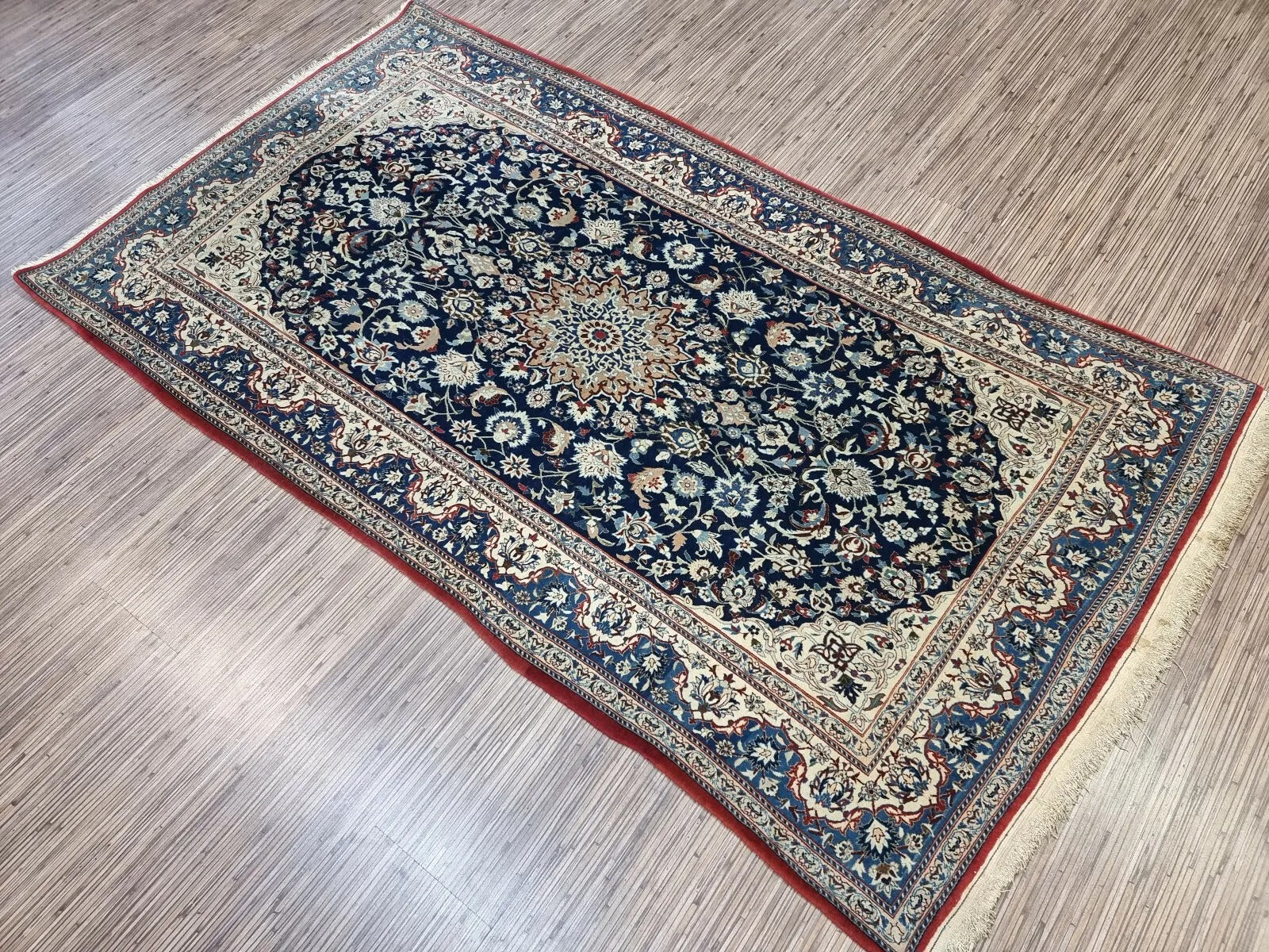 Full view of an antique hand-knotted Persian Nain rug laid flat, showing its rectangular shape, multiple borders, and classic all-over floral pattern with a central medallion.

