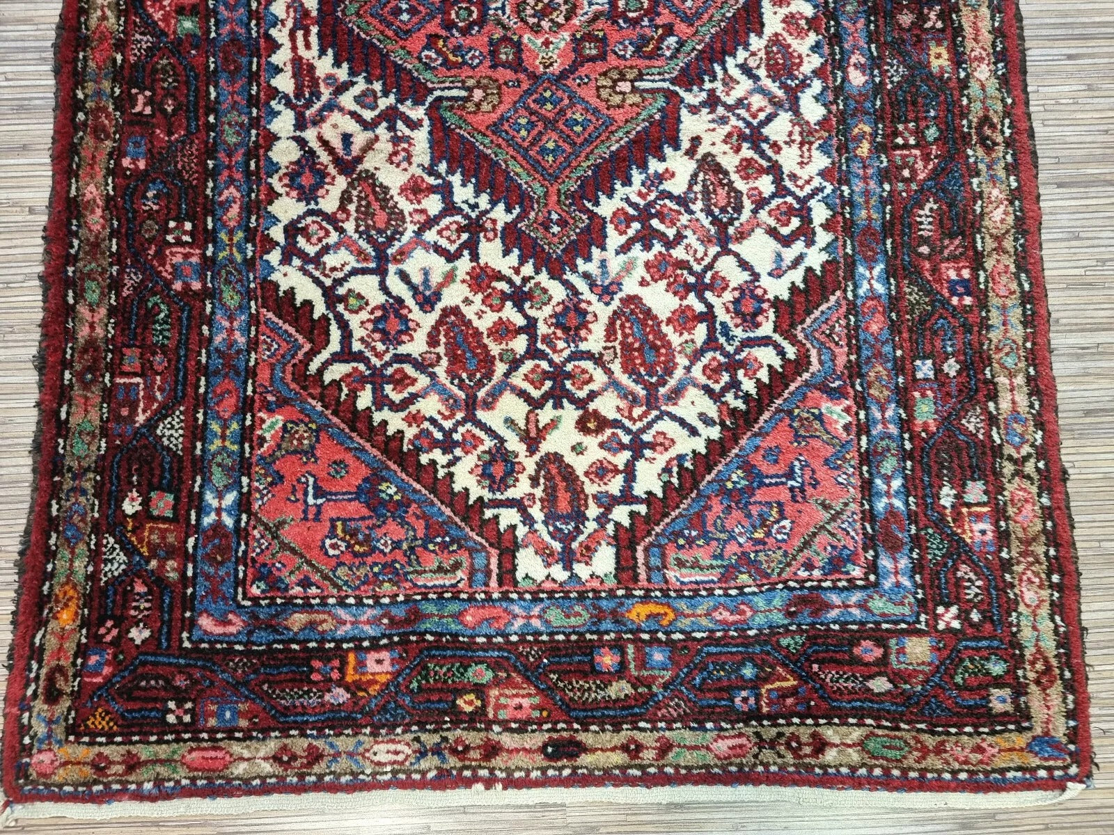 Detail of the central medallion on a vintage Persian Hamadan rug, showcasing intricate floral and geometric motifs typical of Hamadan craftsmanship, with warm red and navy coloration.

