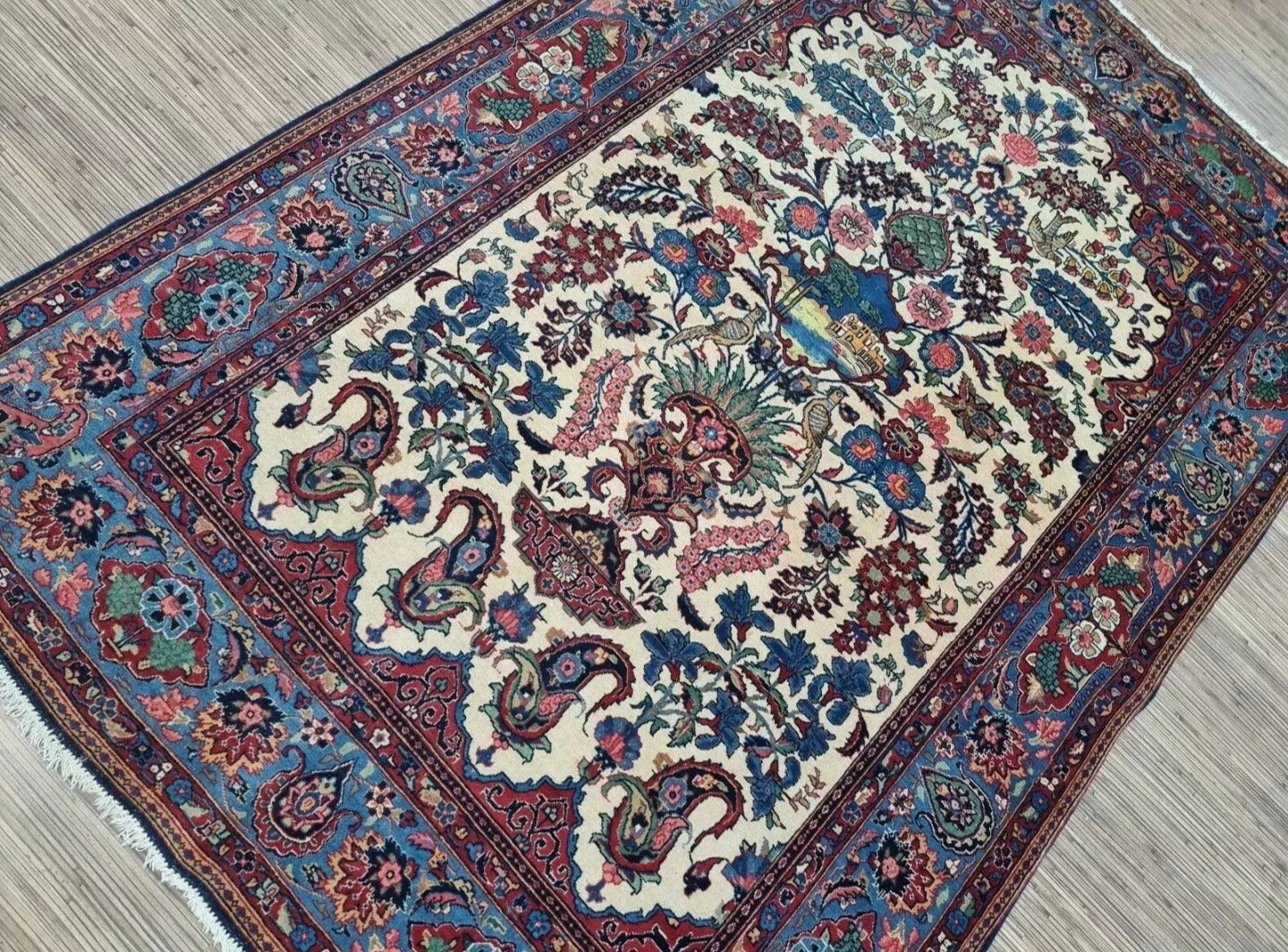 Close-up of a 1920s Persian Kashan carpet showing the detailed central medallion with floral arabesques and vine scrolls in soft beige, navy, and cream tones, with high knot density for intricate detailing.

