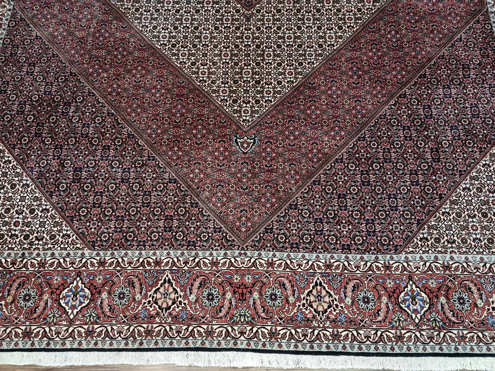 Detail of the central medallion on a vintage Persian Bidjar rug, showcasing intricate floral and geometric motifs typical of Bidjar's weaving heritage, with warm red, navy blue, and cream coloration.


