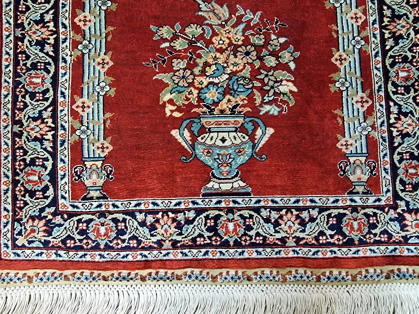 Close-up of a 1970s Turkish Hereke silk carpet showing the fine detailing of traditional floral and medallion motifs in rich red, gold, ivory, and blue, with the characteristic lustrous finish of pure silk pile and foundation.


