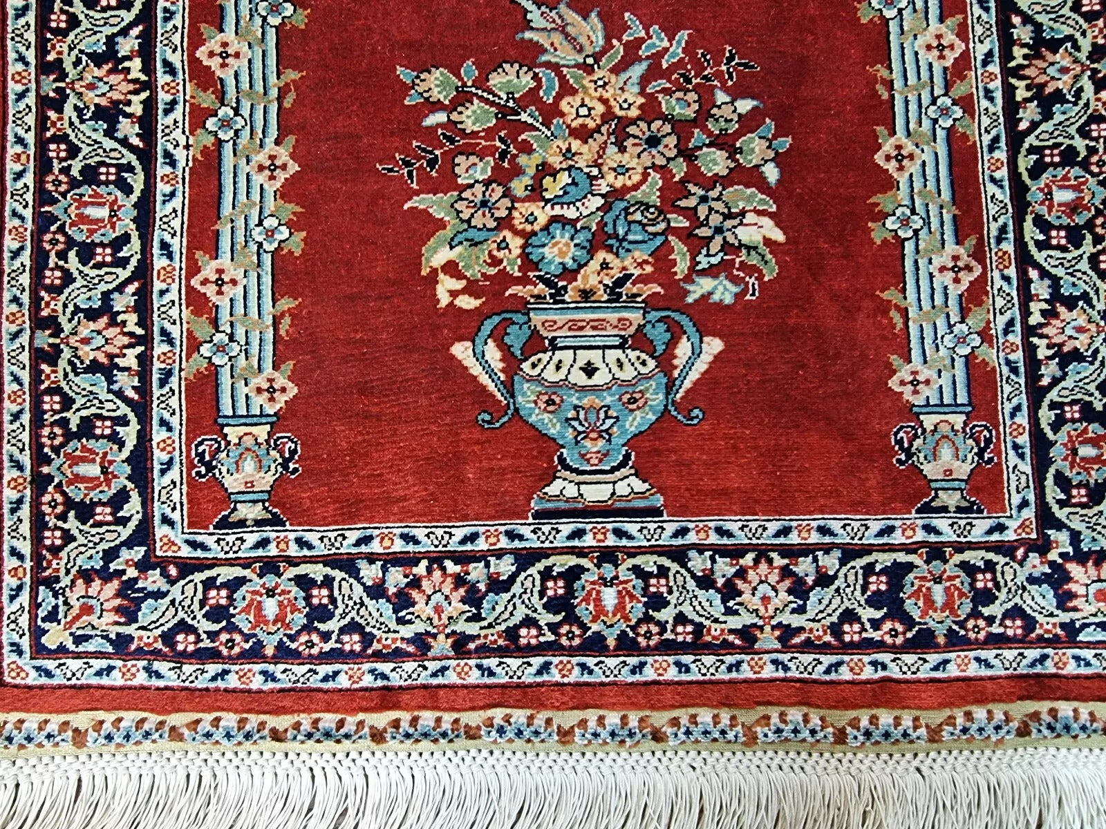Close-up of a 1970s Turkish Hereke silk carpet showing the fine detailing of traditional floral and medallion motifs in rich red, gold, ivory, and blue, with the characteristic lustrous finish of pure silk pile and foundation.

