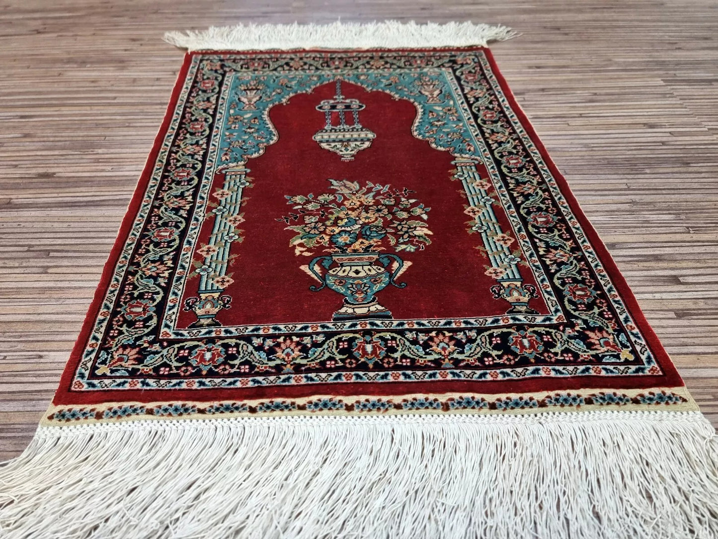 Full perspective of a vintage Hereke silk rug displayed as a wall hanging, demonstrating its 13 × 17 inch size as an elegant accent for enhancing room ambiance.

