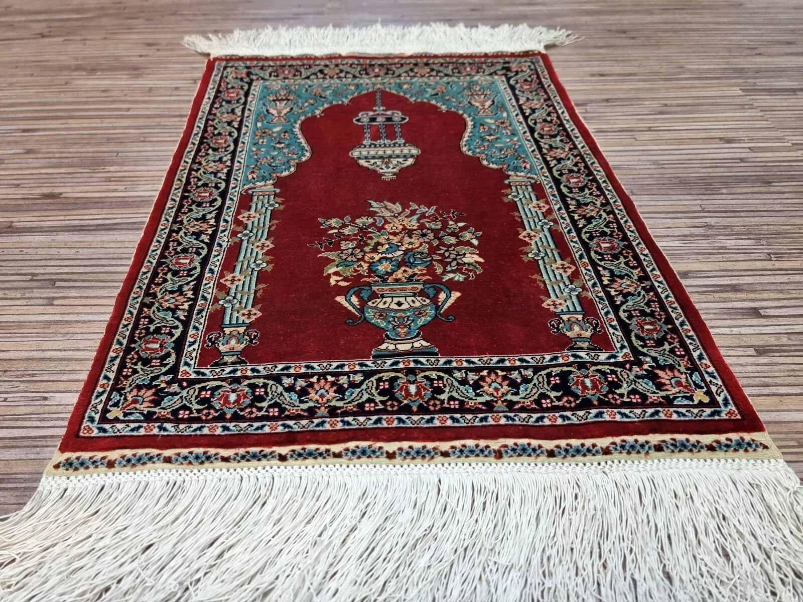 Full perspective of a vintage Hereke silk rug displayed as a wall hanging, demonstrating its 13 × 17 inch size as an elegant accent for enhancing room ambiance.

