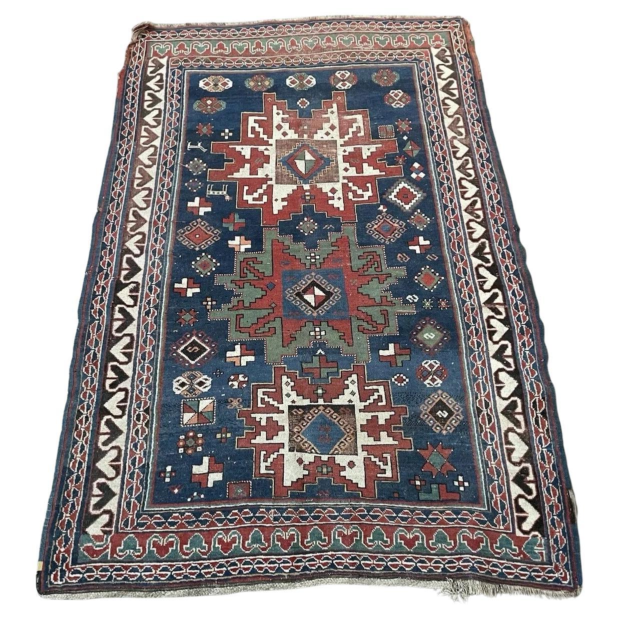 Full top view of the antique Caucasian Lezgi rug showing the central medallion on a blue field.

