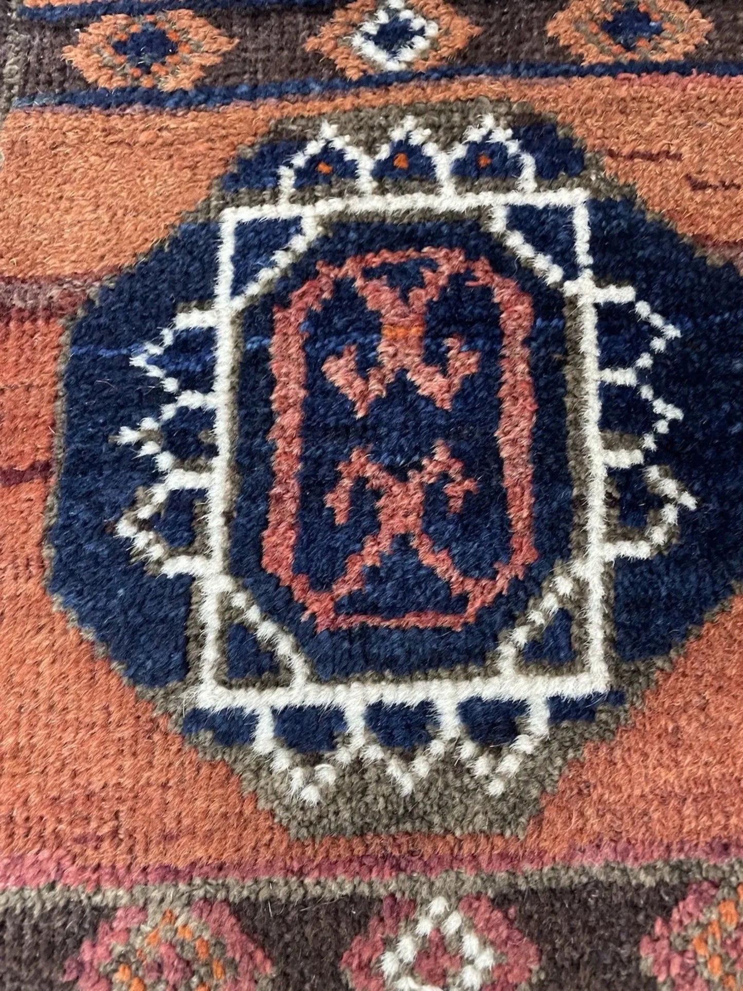Close-up detail of the terracotta field and wool texture in the antique rug.


