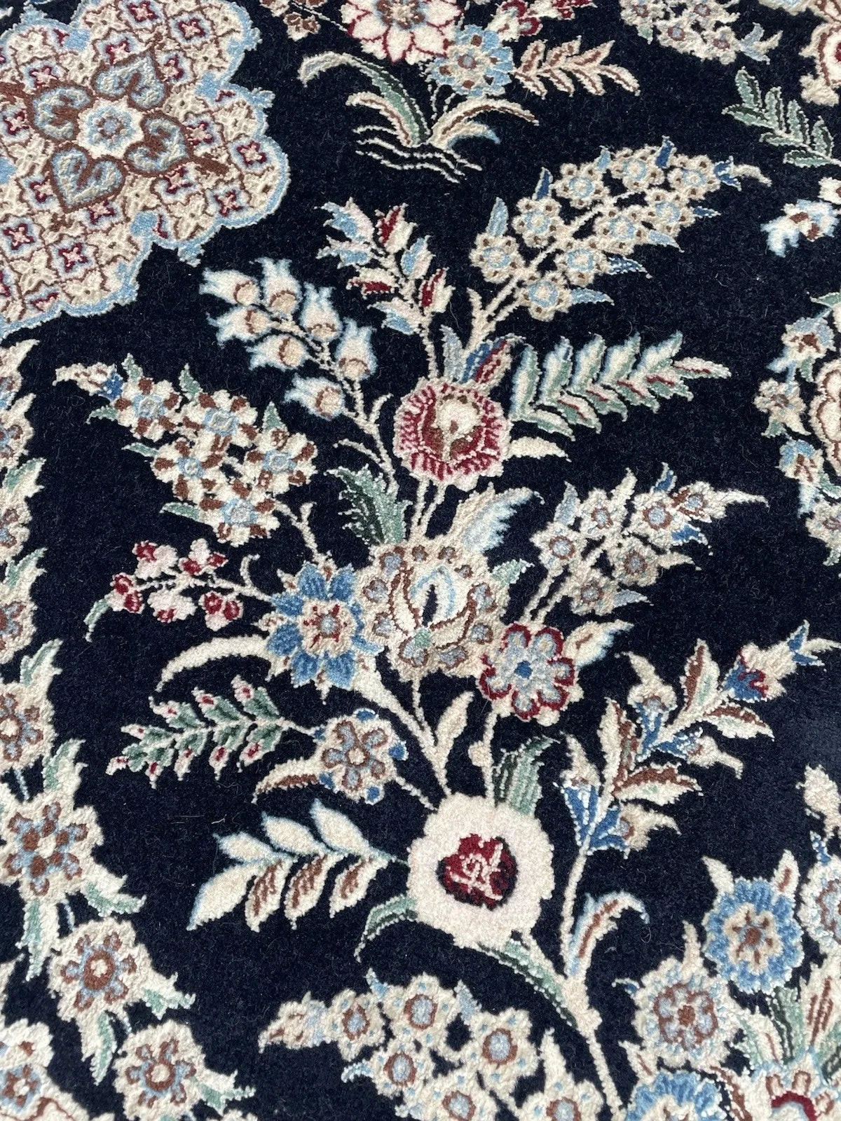 Deep navy vintage Persian rug with central ivory medallion, arabesques, and soft blue and burgundy floral motifs.

