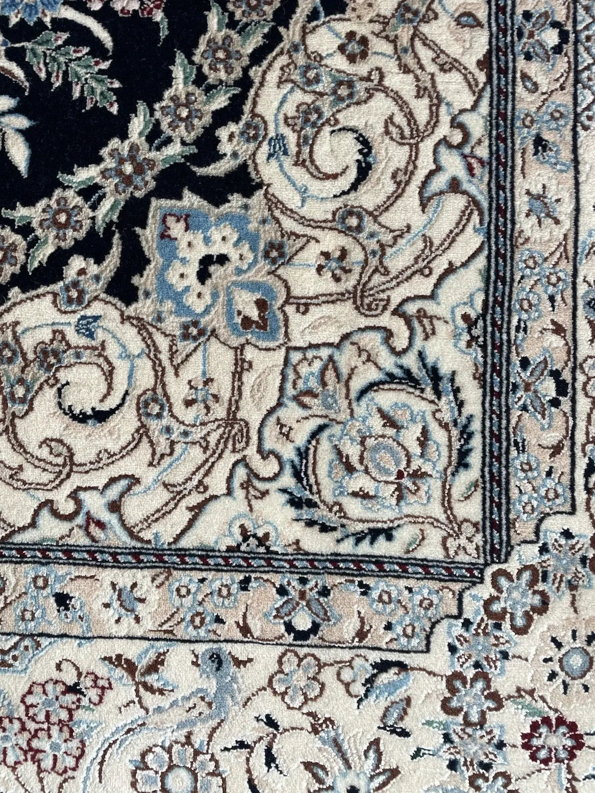 1960s Persian Nain rug with dense floral patterns, scrolling vines, and a light ivory border framing a navy background.

