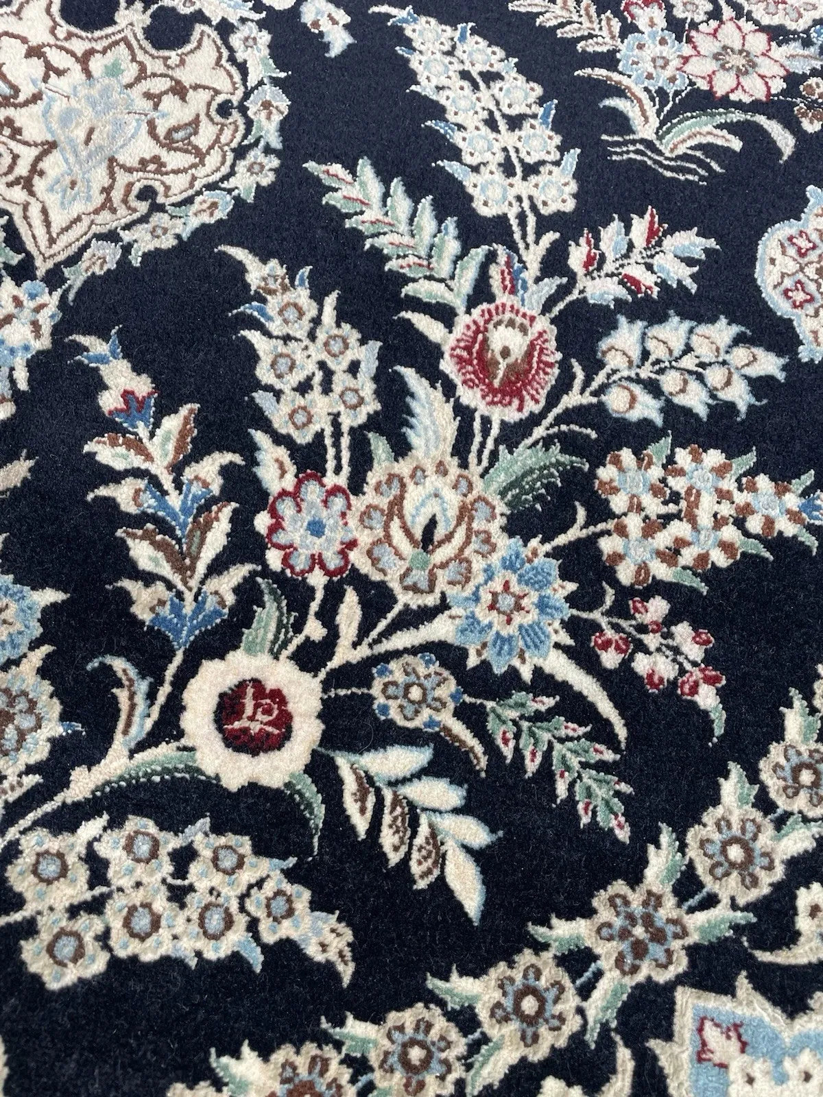 Close-up of delicate arabesque and stylized flower details on a handmade vintage Persian Nain wool rug.

