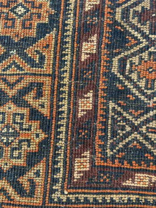 Warm earthy antique Baluch rug in deep brown, camel, ivory, and dark navy tones, hand-knotted in Afghanistan circa 1920.

