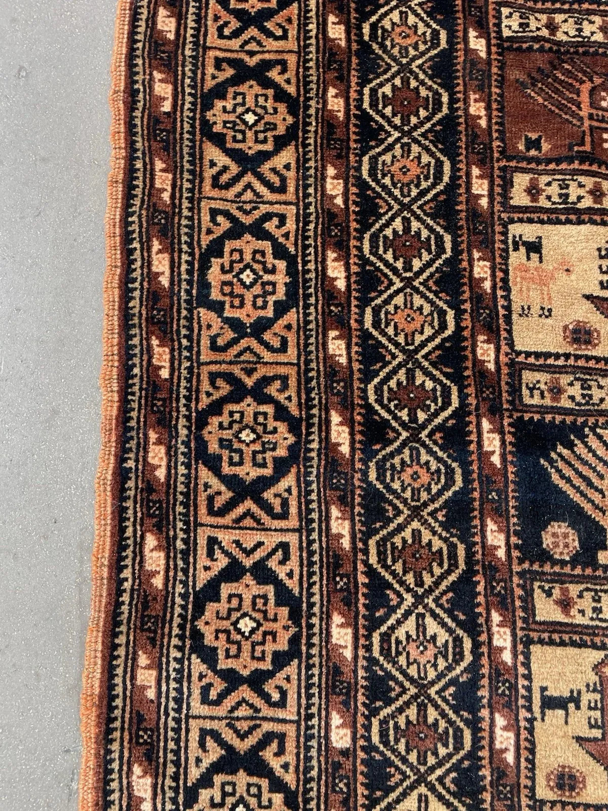 Close-up of stylized animals, birds, and tree-of-life symbols woven into the horizontal bands of an antique Baluch tribal rug.

