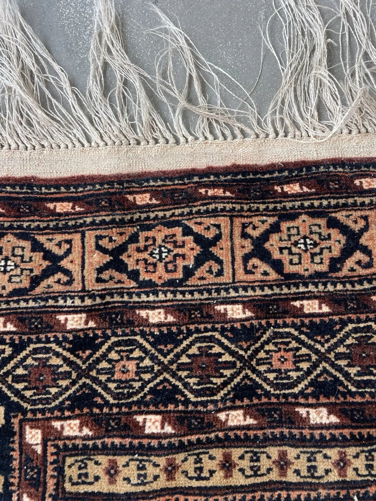 Antique tribal rug showing repeating symbolic motifs including quadruped animals and abstract floral elements in deep brown and ivory.

