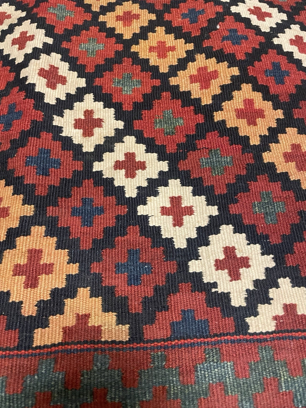 Full view of a Qashqai bagface kilim with an inner guard of ivory kochanak hook motifs on black, a crimson main border, and an olive green reciprocal sawtooth outer perimeter.

