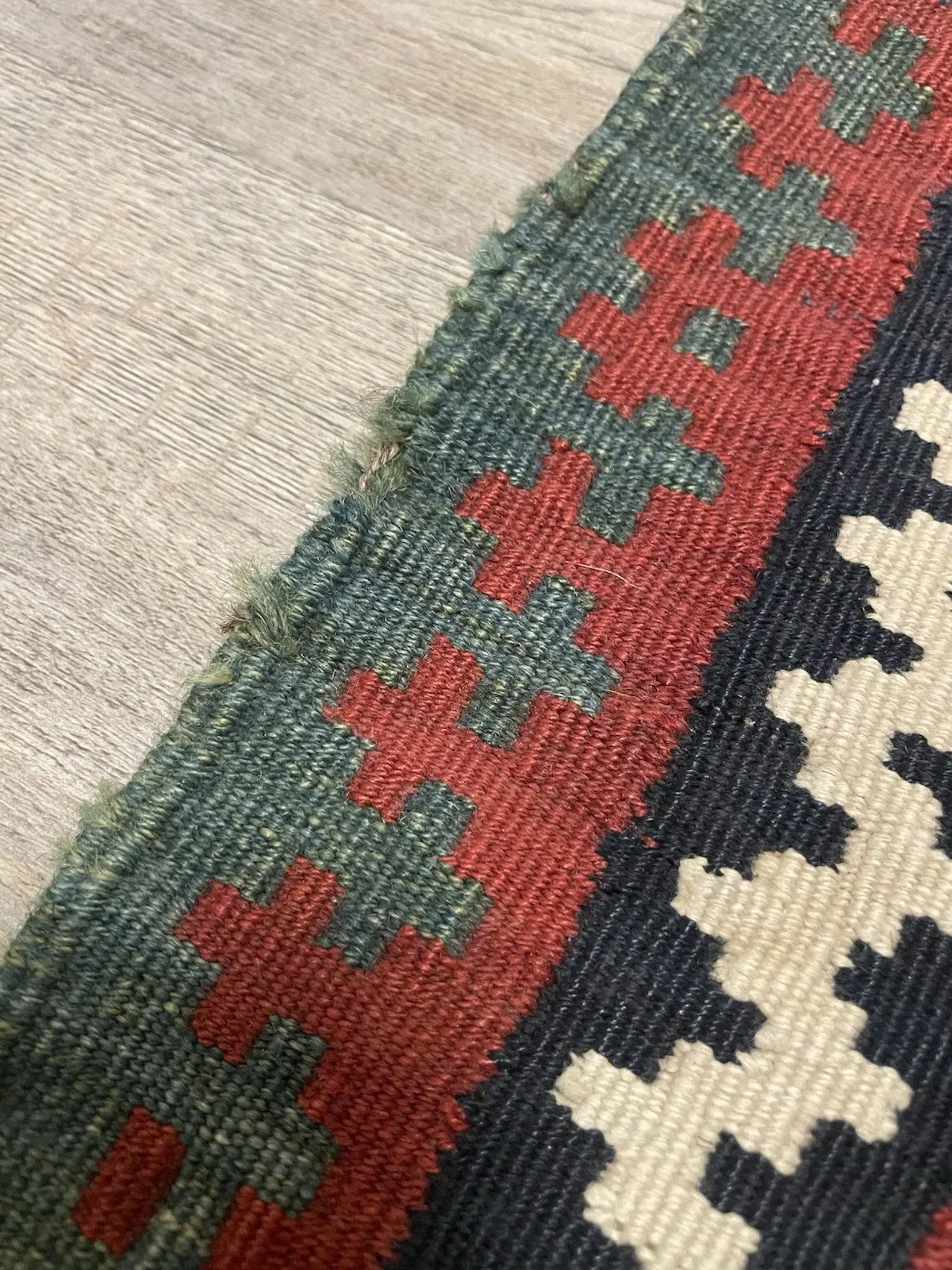 Close-up of a small-format antique Qashqai flatweave showing a precise diagonal grid of small diamonds, each containing a cross or lozenge motif, on a deep black field with a multi-register border system.

